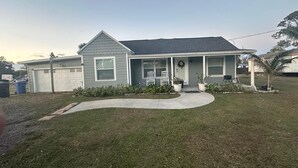Une maison de plain-pied avec un garage, un porche à l’avant orné d’une guirlande et un petit jardin.