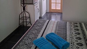 Quarto pequeno e estreito com cozinha compacta, tapete estampado e dois toalhas azuis no chão.