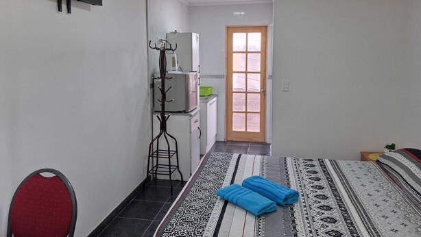 Quarto de hotel com cama, televisão na parede, cabideiro, cozinha compacta e porta que dá para outro quarto.