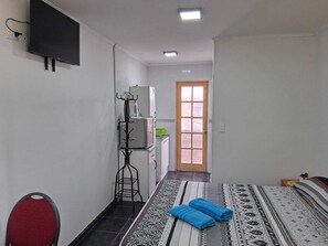 Une chambre d’hôtel comprenant un lit, un téléviseur fixé au mur, un porte-manteau, une kitchenette et une porte donnant sur une autre pièce.
