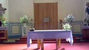 Interior de igreja com altar de madeira, mesa branca e estátuas religiosas.