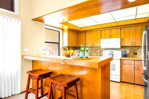 Eine kompakte Küche mit Holzausstattung, einem weißen Kühlschrank, einem Herd und einer Bar mit Sitzgelegenheiten.