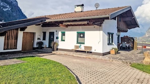 Perinteinen alppimaja, jossa on tiilikatto, puuovi ja pieni patio, jossa on penkki.