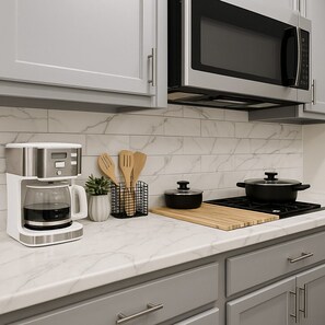 A modern kitchen with a coffee maker, wooden utensils, a pot, and a microwave.