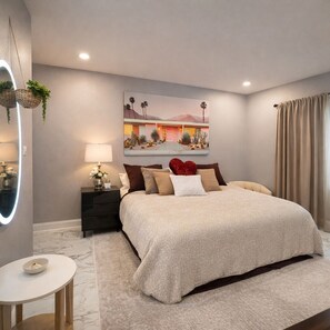 Ein Schlafzimmer mit einem großen Bett, einem Nachttisch mit Lampe, einem wandmontierten Spiegel und einem Gemälde einer Wüstenlandschaft.