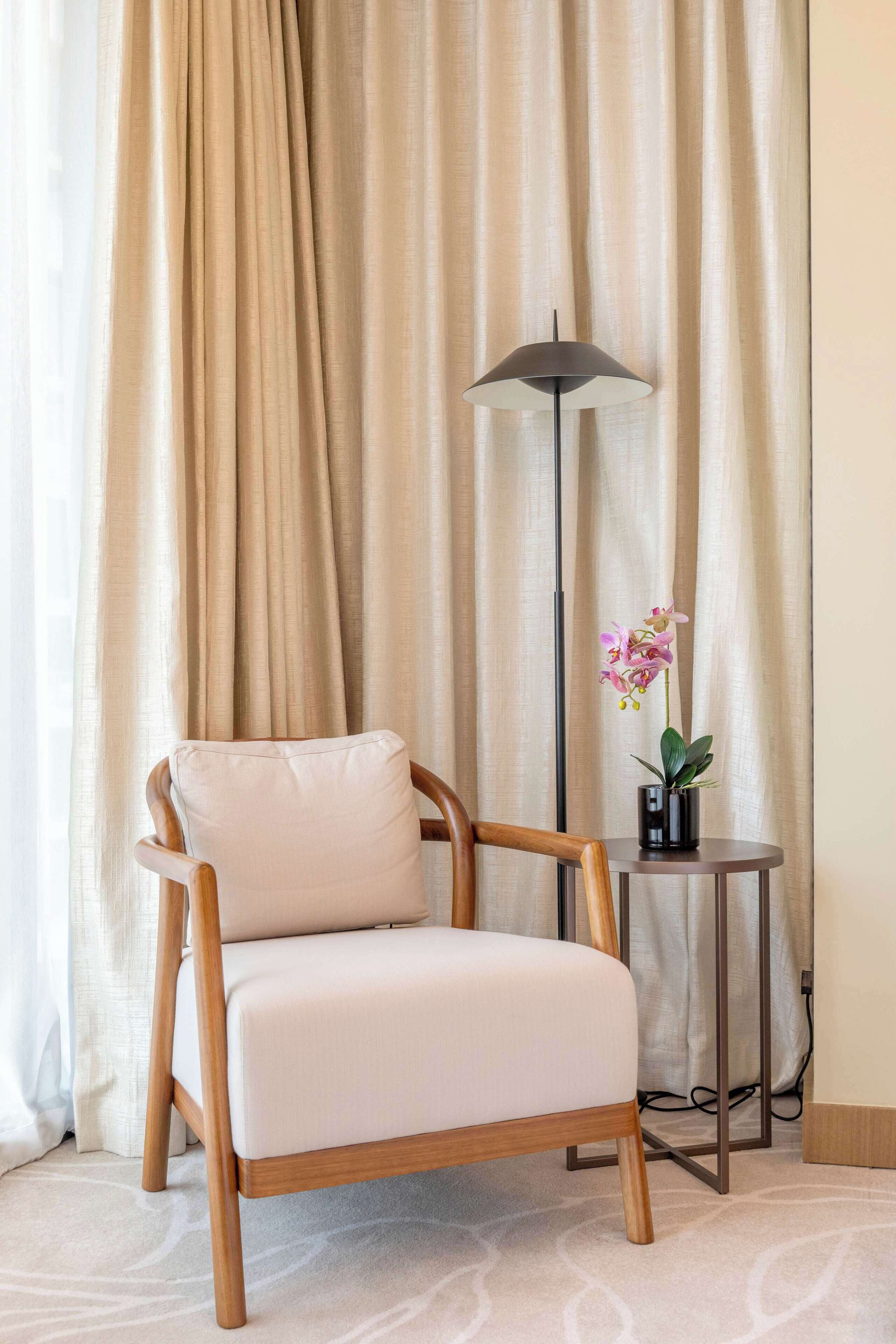 Une pièce comprenant une chaise en bois, un lampadaire et une petite table sur laquelle est posée une orchidée en pot.