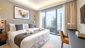 A modern hotel room with a large bed, a desk, and a view of the cityscape. - Address Dubai Opera Residences I 2BR Deluxe Suite (Dubai)