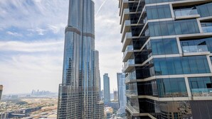 Un edificio de gran altura con un diseño distintivo que se estrecha, rodeado de otras estructuras modernas y un área ajardinada con senderos y vegetación.