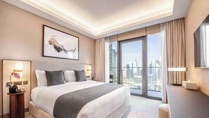 Habitación de hotel con una cama grande, un escritorio, una silla, vista a la ciudad y una obra de arte enmarcada en la pared.