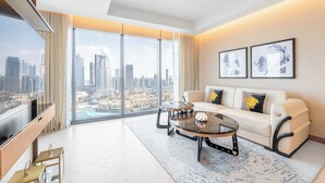 Un salón amplio con un gran ventanal que ofrece vistas a la ciudad, un sofá blanco con cojines decorativos, una mesa de centro y un televisor de pantalla plana.