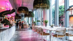 Un interior de restaurante moderno con techos altos, plantas colgantes y una combinación de mesas dentro y fuera.