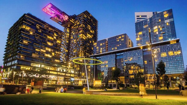 Un horizonte urbano moderno con rascacielos, una plaza pública y una estructura circular distintiva con iluminación.