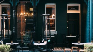 Un área de asientos al aire libre con mesas y sillas, un letrero que indica Gin Lane y la entrada a un bar.