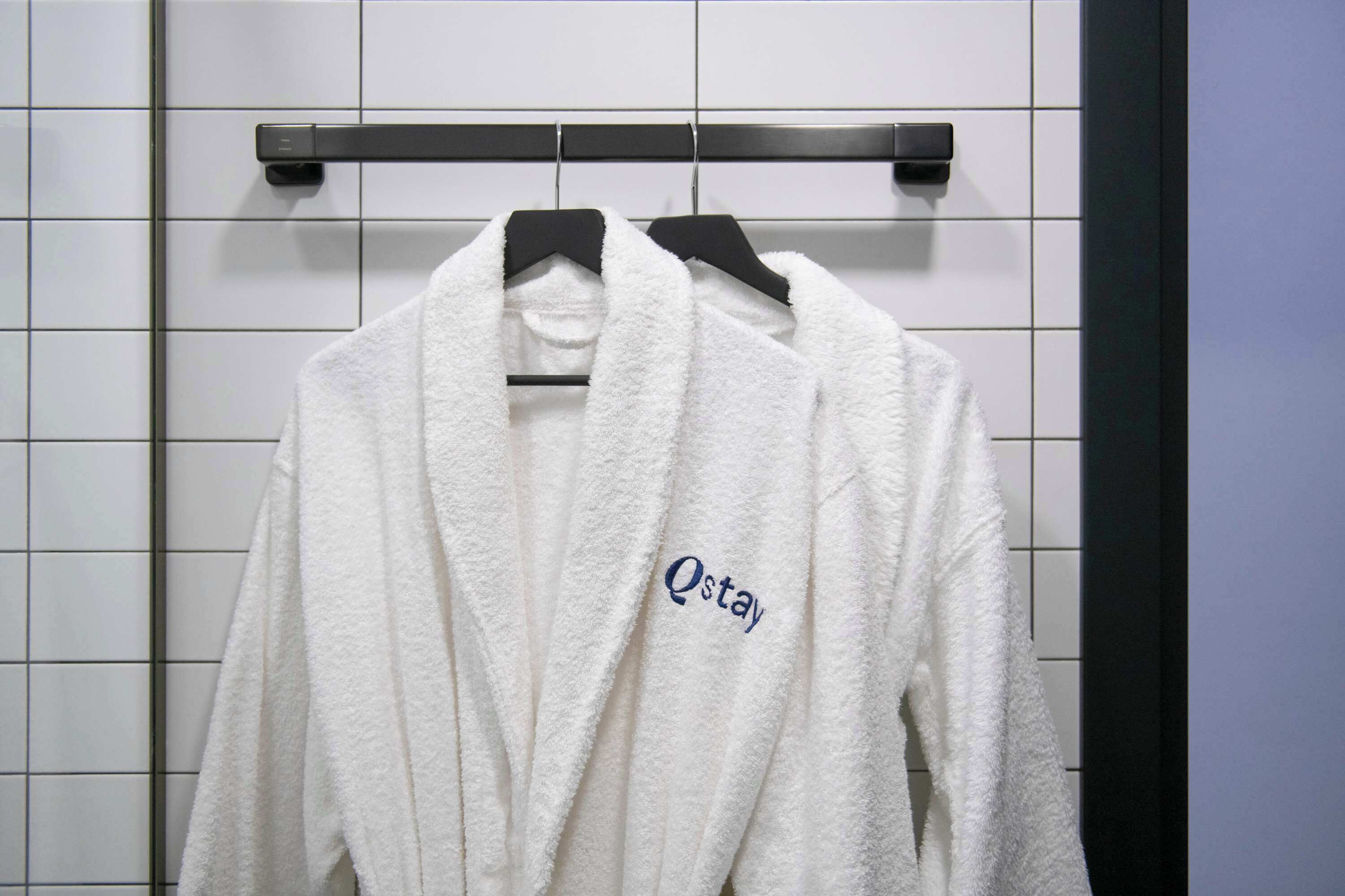 Ein weißes Handtuch mit dem Aufzug "Qstay" an einem Haken hängend.