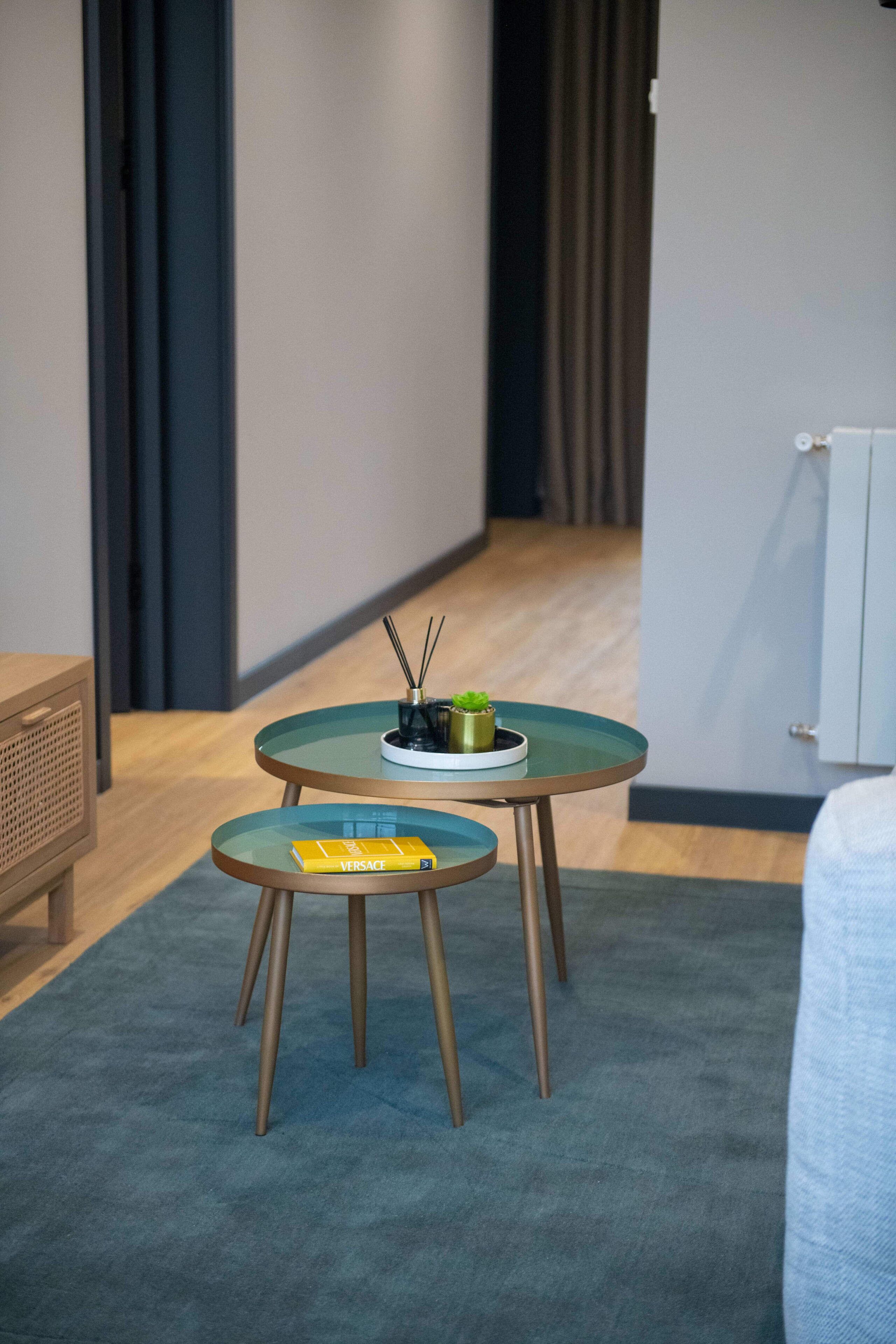 Ein kleines Zimmer mit einem runden Tisch und passendem Hocker, einer kleinen Topfpflanze und einer Duftschachtel von Versace.