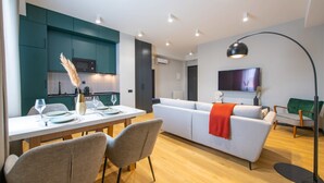 Een moderne woonkamer met een witte bank, een eettafel met borden en glazen, turquoise kastjes en een aan de muur bevestigde televisie.