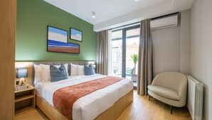 Hotelkamer met een groot bed, een stoel, een nachtkastje en een raam met gordijnen.