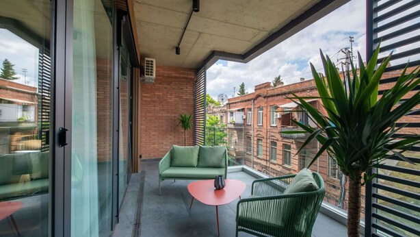Een balkon met een groene bank, een klein rond tafeltje en een groene stoel.