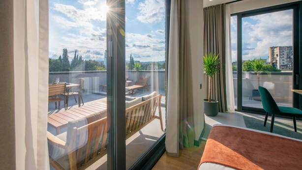 Ein modernes Hotelzimmer mit großem Balkon, einer Essecke und Blick auf die Stadt.