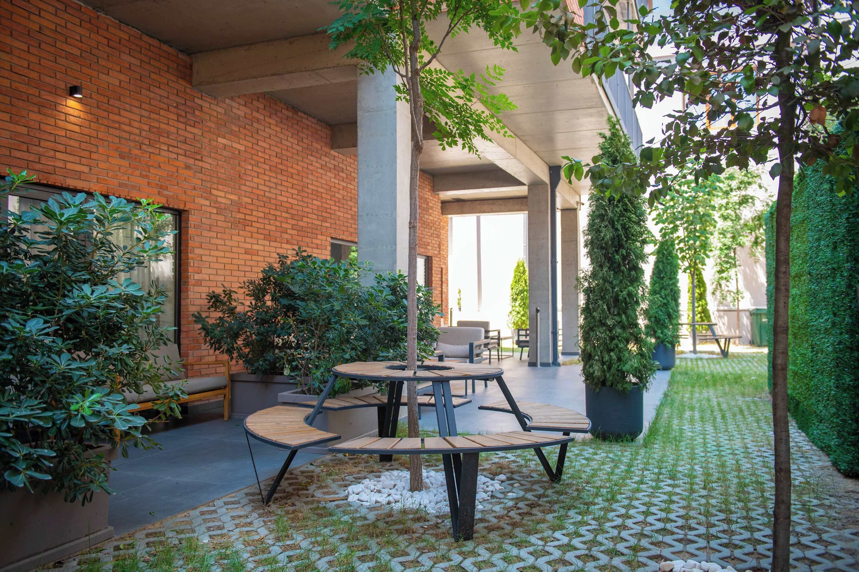 An outdoor patio area with round wooden tables and chairs, surrounded by potted plants and a brick wall.