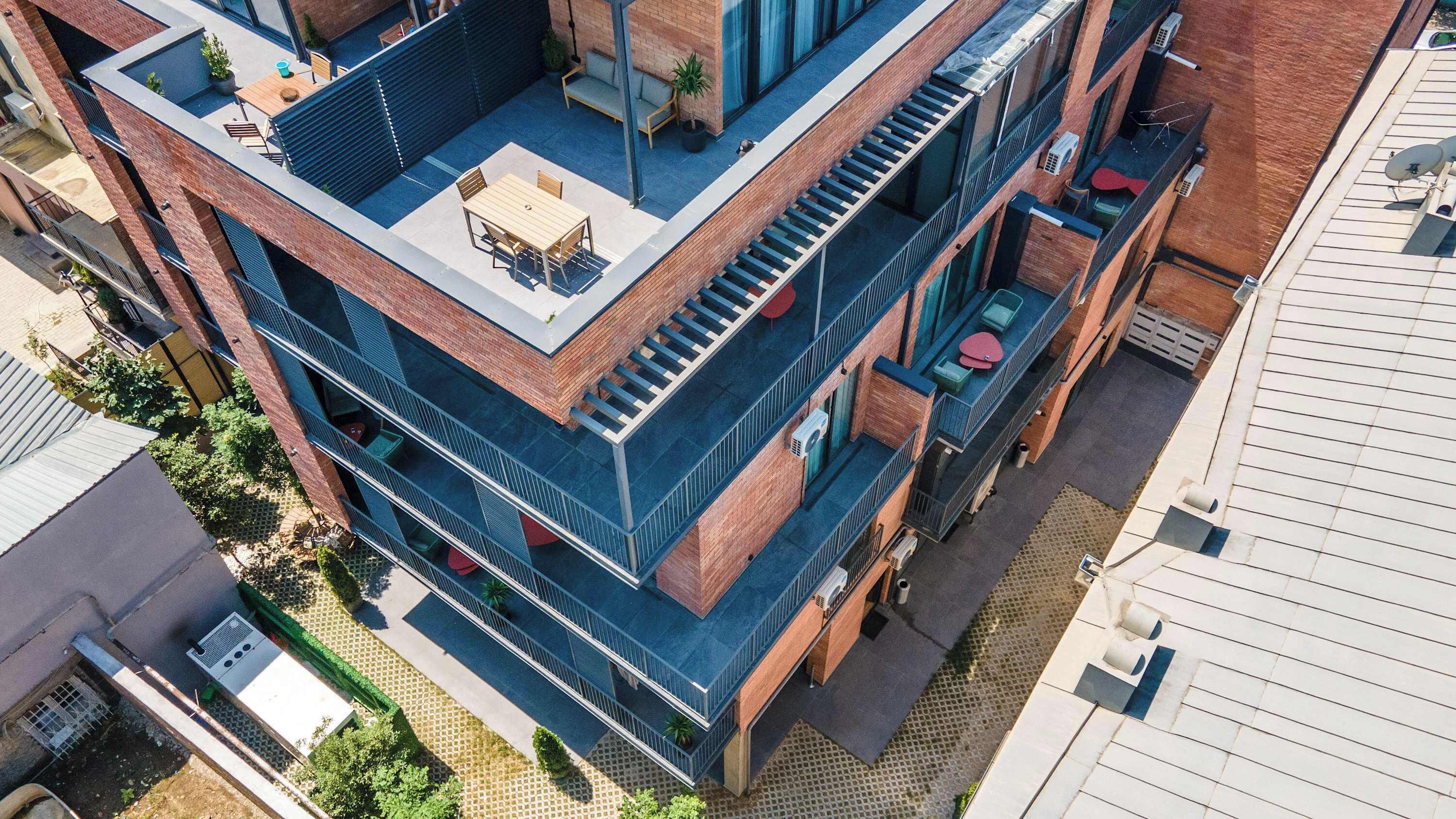 Un immeuble à plusieurs étages doté d’une terrasse sur le toit, d’un espace extérieur aménagé pour s’asseoir et d’une architecture moderne.