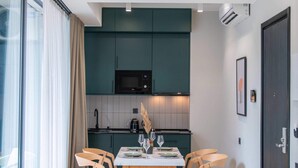 Een moderne keuken met donkergroene kastjes, een houten eettafel met vier stoelen en een groot raam met gordijnen.