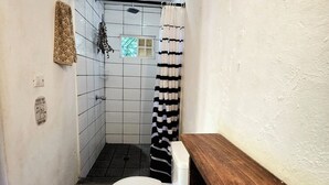 A compact bathroom with a white toilet, a shower with a striped curtain, and a wooden vanity. - 4 Amigos - Seaview Room OLITA, 5 min to the beach, pool, private bathroom (El Zonte)