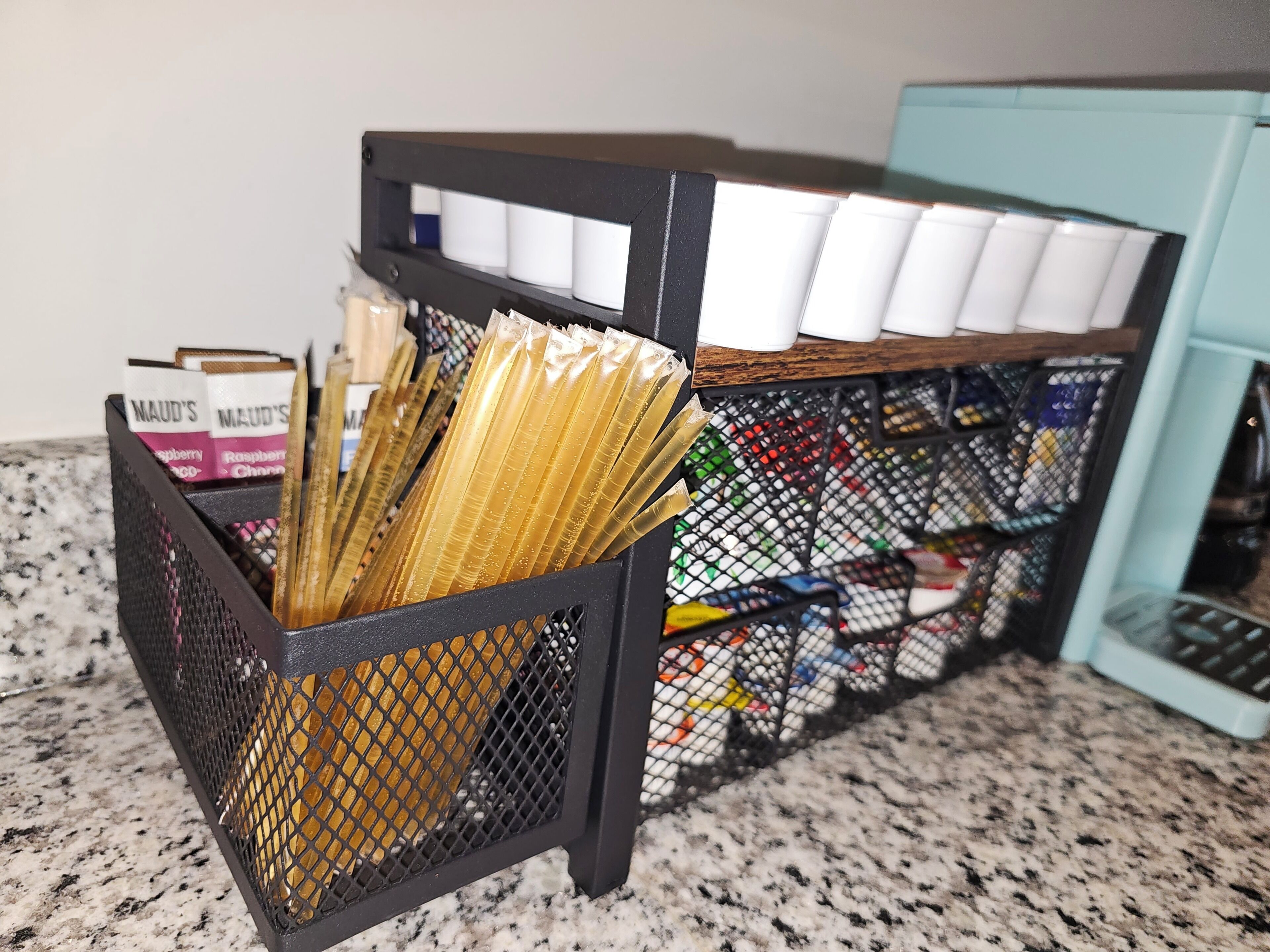 A kitchen counter with a black mesh basket containing various items, a white container with white objects, and a blue appliance.