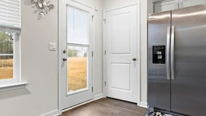 A kitchen with a stainless steel refrigerator, white double doors, and a window with blinds.