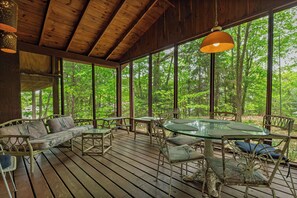 Une terrasse en bois avec une table et des chaises en verre, entourée de grandes fenêtres donnant sur la forêt.
