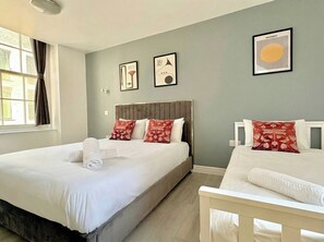 Une chambre d’hôtel avec un grand lit, un plus petit lit et une fenêtre avec des rideaux.