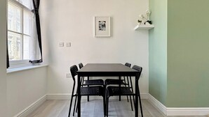 Ein Essbereich mit Tisch und Stühlen, einem Fenster mit Vorhängen, einem Wandbild und einer Wand in Grünton.