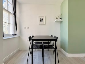 Un coin repas avec une table et des chaises, une fenêtre avec des rideaux, un tableau accroché au mur et un mur d’accent de couleur verte.