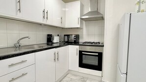 Eine moderne Küche mit weißen Schränken, einer Edelstahl-Dunstabzugshaube, einem Gasherd, einem Backofen und einem Kühlschrank, sowie einer schwarzen Arbeitsplatte.
