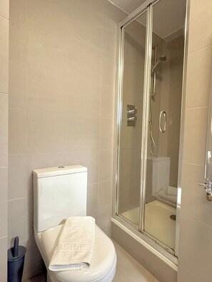 Ein Badezimmer mit Toilette, einer Duschkabine aus Glas und einem Handtuch auf dem Sitz.
