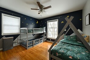 Quarto de criança com beliches, ventilador de teto e adesivos de estrelas nas paredes.