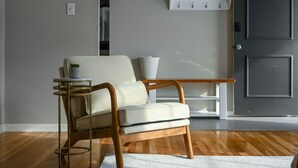 A modern living room with a wooden floor, a beige armchair, a small side table, and a white console table against a grey wall. - Relaxing Space for Families & Friends — Sleeps 10 + Pet-Friendly (Grandview)