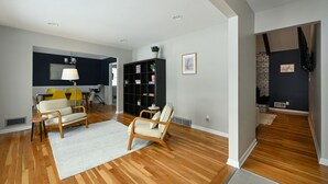 A spacious living area with wooden flooring, a sofa, a chair, and a bookshelf. - Relaxing Space for Families & Friends — Sleeps 10 + Pet-Friendly (Grandview)