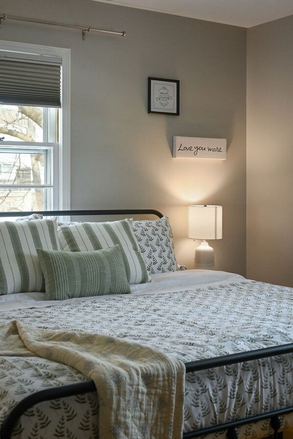 A bedroom with a bed, pillows, a bedside lamp, a framed picture, and a window with blinds. - Relaxing Space for Families & Friends — Sleeps 10 + Pet-Friendly (Grandview)