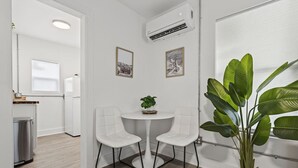 Ett modernt, minimalistiskt rum med två vita stolar runt ett litet bord, en krukväxt och inramade bilder på väggen.