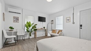 Ett modernt, minimalistiskt sovrum med en stor säng, ett skrivbord med en stol, en soffa och en TV som är monterad på väggen.
