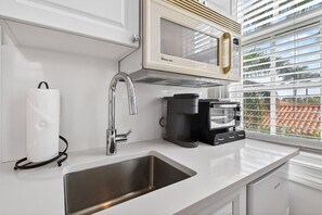A kitchen with a stainless steel sink, a coffee maker, a microwave, and a paper towel dispenser. - Lavender Orchid - Palm Beach Historic (Palm Beach)