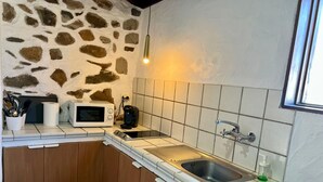 Eine kleine Küche mit Steinwand, einer Mikrowelle, einem Wasserkocher, einer Spüle und einem Fenster.