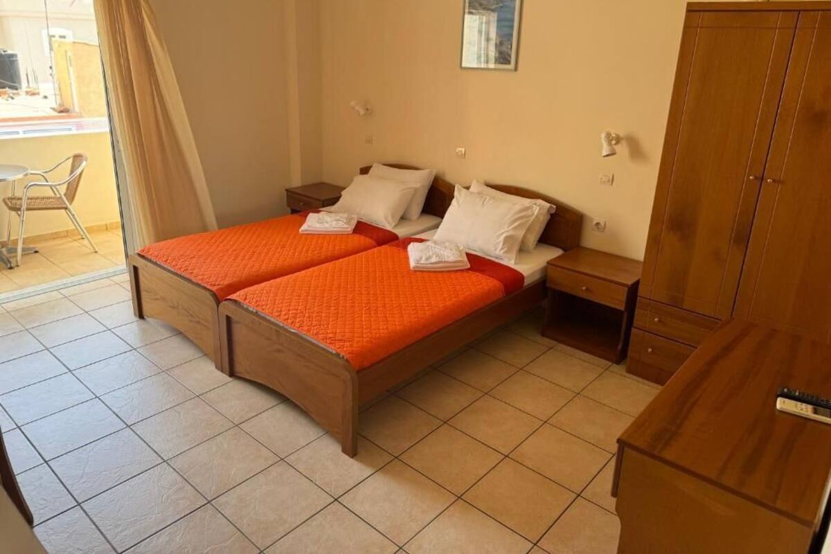 Ein Doppelbett mit orangefarbener Bettdecke, ein Holzschrank, ein Nachttisch und ein Stuhl.
