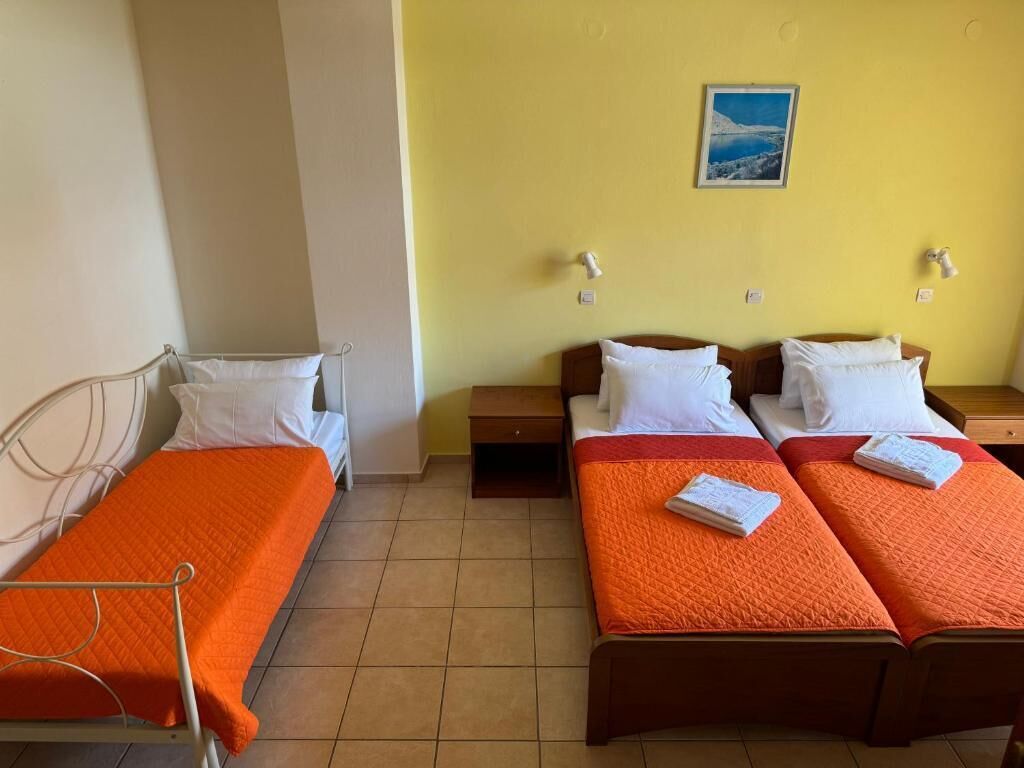 A room with two single beds and two double beds, each with white linens and orange blankets.