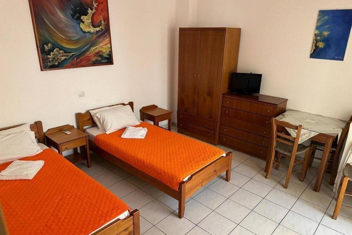 Ein Zimmer mit zwei Holzbetten, einem Schrank aus Holz, einem Schreibtisch mit Stuhl sowie einem Fernseher auf einem Holzschrank.