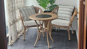 Ein Zimmer mit einem runden Tisch, zwei Korbstühlen, einer Topfpflanze und einem Deckenventilator.