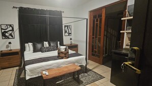 Una camera da letto con un letto a baldacchino, un comodino in legno, un tavolino da notte, una panca e una porta con un pannello di vetro.
