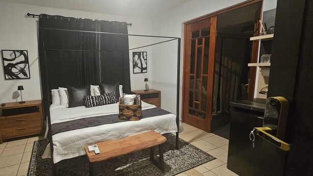 Ein Schlafzimmer mit einem Himmelbett, einem Nachttisch aus Holz, einem Beistelltisch, einer Bank und einer Tür mit Glasfenster.