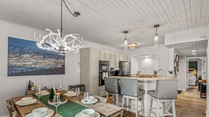 Eine moderne Küche mit weißen Schränken, eine Essecke mit einem Holztisch, gedeckt für vier Personen, und ein großes Bild an der Wand.